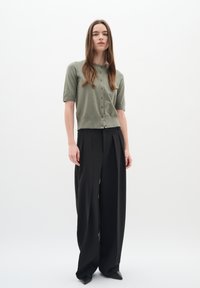 Cardigan verde chiaro a maniche corte con bottoni abbinato a pantaloni neri a vita alta e a gamba larga. Tessuto morbido e vestibilità comoda.