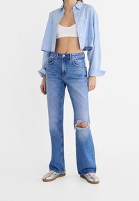 Blue striped cropped shirt, white bralette, distressed light blue flared jeans, and silver sneakers with a tan sole.