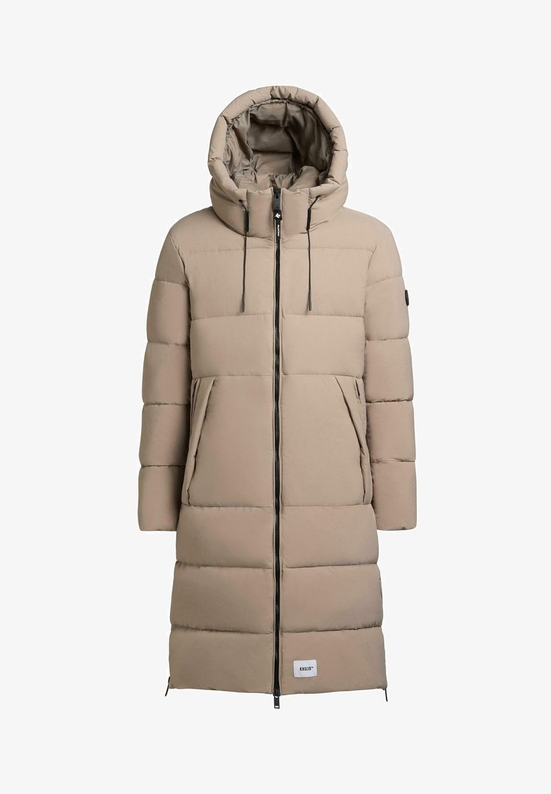 Beige polstret frakk med høy krage og hette, med full front glidelås, store lommer, og et logo-patch på den nedre fronten.