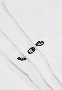 White socks made of textured cotton with ribbed cuffs. Features three black embroidered round logos near the top.