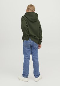 Grön hoodie med en känguruficka, tillsammans med blå raka jeans. Modellen har på sig vita sneakers och vänder ryggen mot kameran.