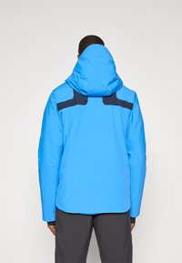 Casaco azul impermeável com capuz, apresentando detalhes em azul escuro e um design elegante, adequado para atividades ao ar livre.