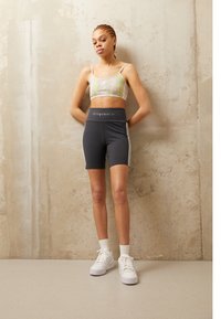 Sporty cropped topp i pastellfarger, kombinert med mørkegrå høytlivshorts med hvite sidestriper og hvite joggesko med strukturerte såler.