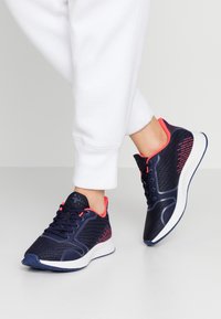 Námořnické sportovní boty s růžovými akcenty, síťovaným svrškem, texturovanými vzory a bílou podrážkou, navržené pro pohodlí a podporu.