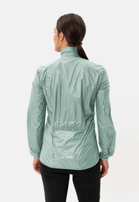 Lichte mintgroene jas met een hoge kraag, elastische taille en een achterzak. Gladde textuur met een glanzende afwerking. Logo op de rug.