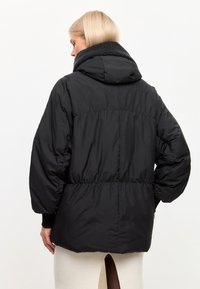 Zwarte pufferjack met capuchon, voorzien van een gestructureerde grijze kraag, elastische manchetten en een getailleerde taille voor een ontspannen pasvorm.