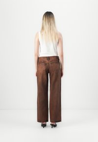 Brown wide-leg jeans with frayed hems, medium wash, featuring back pockets and a textured surface, paired with a white sleeveless top.
