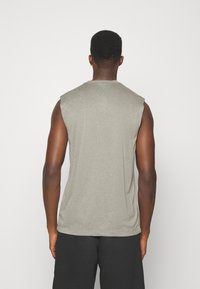 Homme aux cheveux courts portant un débardeur gris et un short noir, vu de dos sur un fond blanc uni.