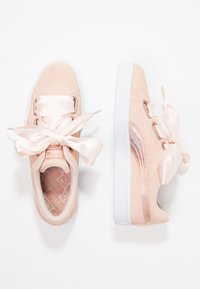 Helle pinke Sneakers mit einer glatten Wildleder-Oberfläche, Satinschleifen-Schnürsenkeln und einem metallischen Akzentstreifen an der Seite, auf einer weißen Gummisohle.
