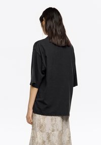 Camiseta negra de corte holgado con cuello redondo y mangas cortas, fabricada en una tela suave que muestra una textura sutil y un ajuste relajado.