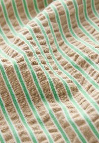 Tissu texturé avec un motif de rayures vertes et blanches sur un fond beige, affichant une apparence légèrement froissée.