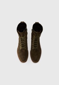 Paire de bottines marron en daim à lacets avec fermetures éclair latérales, vues de dessus sur un fond gris clair.