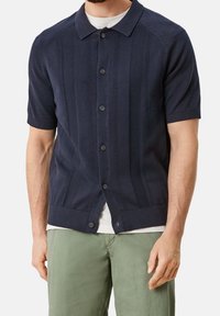 Marineblauwe polo met korte mouwen, gebreid en met een gestructureerd verticaal streep patroon, klassieke kraag en knoopsluiting. Het materiaal lijkt zacht en ademend te zijn.