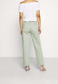 Top blanco ligero, sin mangas, con detalles de ojal, combinado con pantalones verde pastel de tiro alto y pierna recta, y tacones morados claros con tiras.
