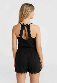 Svart jumpsuit med vågig spetsbak och knytning. Har resårmidja och spetsdetaljer på shortsen. Enkelt, lättviktigt tygdesign.