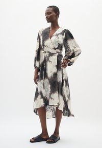 Rochie tip înfășurat, realizată dintr-un material ușor, cu un model ce prezintă nuanțe de negru și crem. Mâneci lungi, talie accentuată cu un brâu și tiv asimetric. Asortată cu sandale negre.