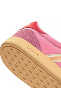 Baskets Adidas roses et rouges avec une semelle beige montrant un motif en losange et des détails en suède perforé sur le côté et le talon.