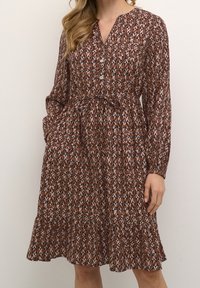 Vestido marrón con estampado, confeccionado con una tela ligera, que presenta un escote en V, cierre de botones, cintura fruncida y un dobladillo con volantes en capas.