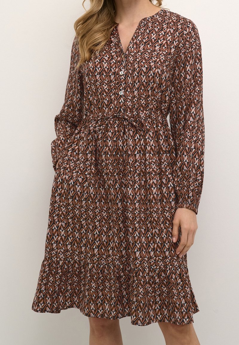 Vestido marrón con estampado, confeccionado con una tela ligera, que presenta un escote en V, cierre de botones, cintura fruncida y un dobladillo con volantes en capas.