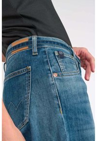 Jeans de mezclilla azul con un corte recto, que cuentan con un diseño de bolsillo trasero, acentos de costura y un parche de cuero en la cinturilla.