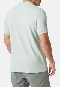 Polo de manga corta en verde menta claro con cuello acanalado, textura sutil y un acento de logo circular en la manga izquierda.