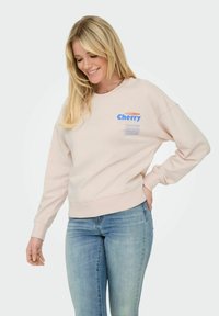 Sweatshirt rose pâle avec un col rond, des bords côtelés aux poignets et au bas. Présente le texte bleu "Cherry" et d'autres détails imprimés sur le devant.