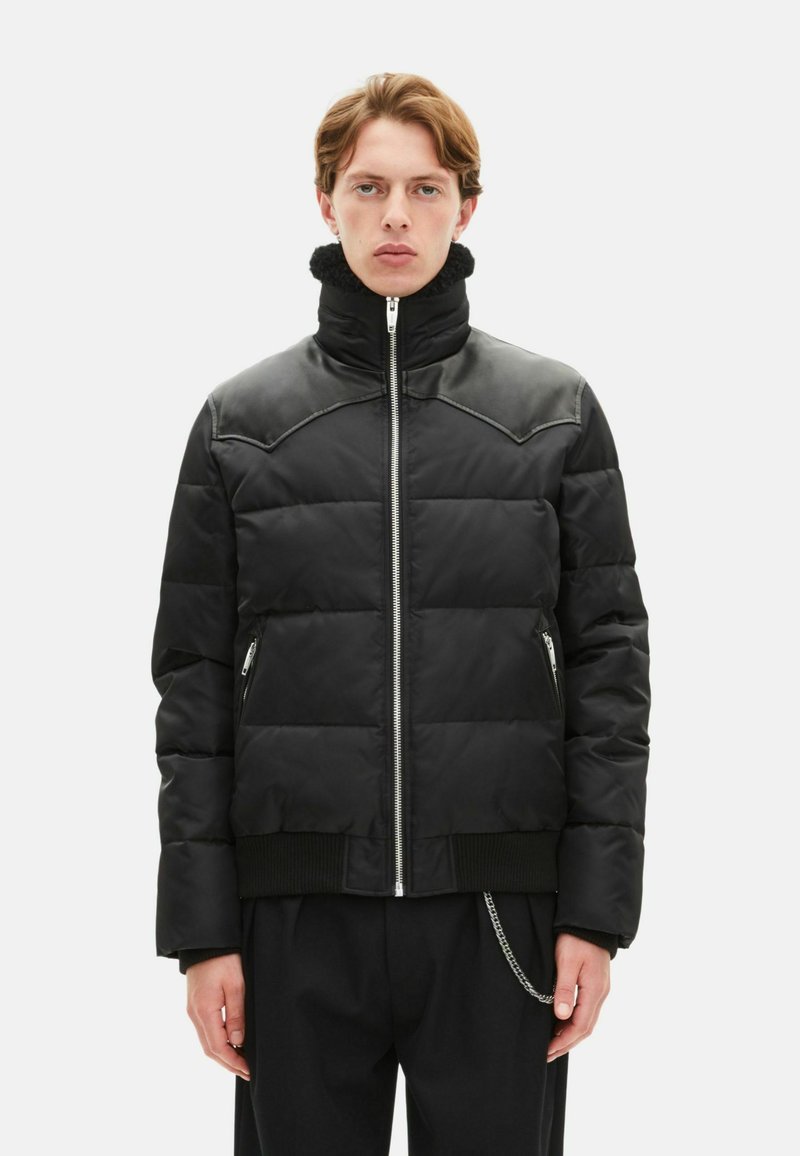 Schwarze gesteppte Jacke mit hohem Kragen, Lederakzenten an den Schultern, Reißverschlusstaschen und geripptem Saum. Glatte Textur, elegantes Design.