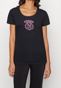 Camiseta negra de mezcla de algodón, con escote redondo y mangas cortas. El diseño frontal incluye un logo rosa con acentos de laurel.