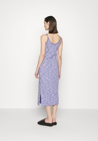Vestido maxi ajustado roxo com um padrão texturizado, alças finas e fenda lateral. Usado com sandálias pretas, visto pela parte de trás.
