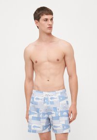 Svømmebukser i lys blå med et blandet mønster av fisk og nautiske design. Elastisk livlinje med snøring. Stoffet ser glatt ut.