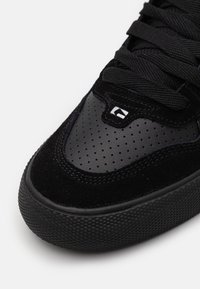 Baskets noires avec un dessus en suède texturé et des accents en cuir lisse, ornées de perforations et de lacets plats noirs. Semelle en caoutchouc striée.