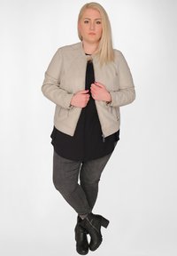 Ljusgrå läderjacka med zipförslutningar, kombinerad med en svart skjorta och mörkgrå jeans. Svarta ankelskor med kraftiga klackar.