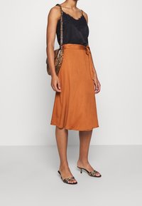 Woman wearing black lace-trim camisole, rust-colored midi skirt with belt, leopard print heeled sandals, and matching snake-pattern shoulder bag.