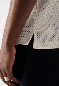 Top in maglia di un delicato crema con un design testurizzato a trama aperta. Presenta spacchi laterali e una vestibilità rilassata, abbinato a pantaloni in denim scuro.