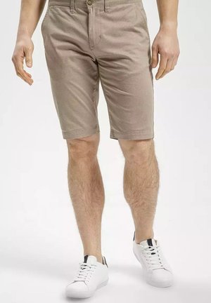 Beżowe bawełniane szorty o teksturowanym splocie, z zapięciem na guzik, bocznymi kieszeniami i prostym krojem, zestawione z białymi trampkami.