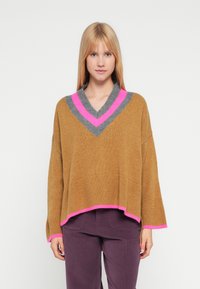 Pull marron en tricot avec un col en V, pr�ésentant des accents gris et rose vif sur le col et l'ourlet. Coupe ample avec des manches longues.