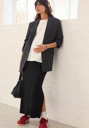 Svart kjol med sidohalk, vit topp och grårandig blazer. Röda sneakers och en svart väska fulländar outfiten. Mjuka texter och skräddarsydd passform.