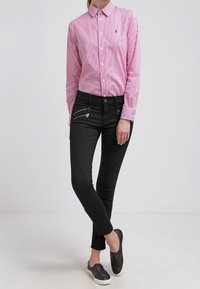 Červeno-bíle pruhovaná bavlněná košile na knoflíky, černé skinny džíny se zipovými akcenty, nošeno s černými slip-on botami.