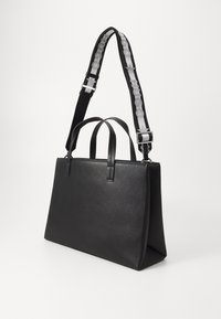 Svart lær tote-bag med to topphåndtak og en avtagbar stropp med et merket vevd design. Glatt, strukturert form med minimalistiske detaljer.