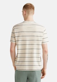 Camiseta de manga corta beige con rayas horizontales grises. Tejido suave, cuello redondo y corte relajado. Diseño sencillo sin logotipos visibles.