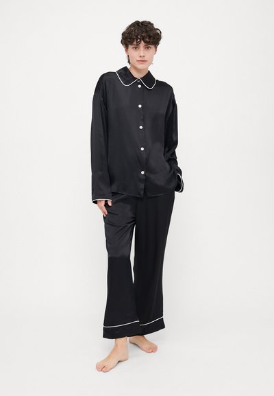 Black satin pajama set featuring a long-sleeve button-up shirt with a collar, and matching pants with white piping at the cuffs.