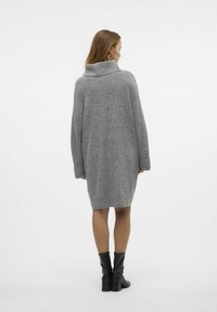 Abito in maglia oversized grigio con alto colletto a scialle, polsini a coste e orlo arrotondato, abbinato a stivali neri con tacco.