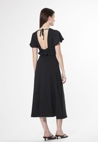 Vestido negro midi con mangas cortas con volantes, espalda descubierta y un lazo en la cintura. Presenta una textura suave y una silueta fluida.