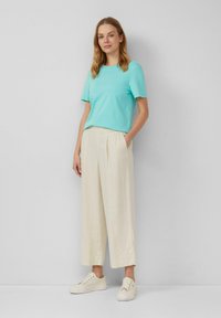 T-shirt azzurro chiaro a maniche corte, pantaloni beige a gamba larga con pieghe frontali e sneakers bianche. Design semplice, texture morbida, vestibilità casual.