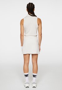 Ljusbeige ärmlös polo och matchande kjol, tillverkad av mjukt tyg. Vita sportstrumpor med svarta detaljer och kraftiga vita skor.