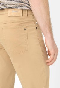 Khaki broek met een subtiele textuur, rechte pasvorm, twee achterzakken met kruissteekdetail en een label op de tailleband.