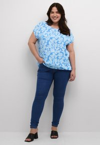 Lyseblå blomstret top med kortærmer, parret med mørkeblå slim-fit jeans og sorte blokhælede mules. Glat stofstruktur.