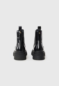 Bottines en cuir verni noir avec une semelle en caoutchouc épaisse, des languettes de tirage et des accents en or sur le talon. Fini de surface lisse et brillant.