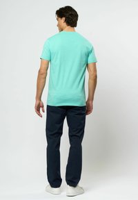 Ljus turkos t-shirt med kort ärm och rund hals, i kombination med mörkblå byxor och vita sneakers, som visar en avslappnad passform.