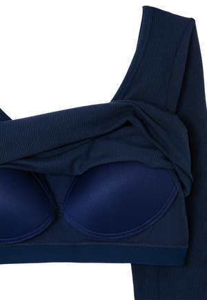 Dunkelblaues, geripptes Stoffkleidungsstück, das teilweise gefaltet ist, um einen passenden gepolsterten BH mit geformten Cups und breiten Trägern darunter zu zeigen.